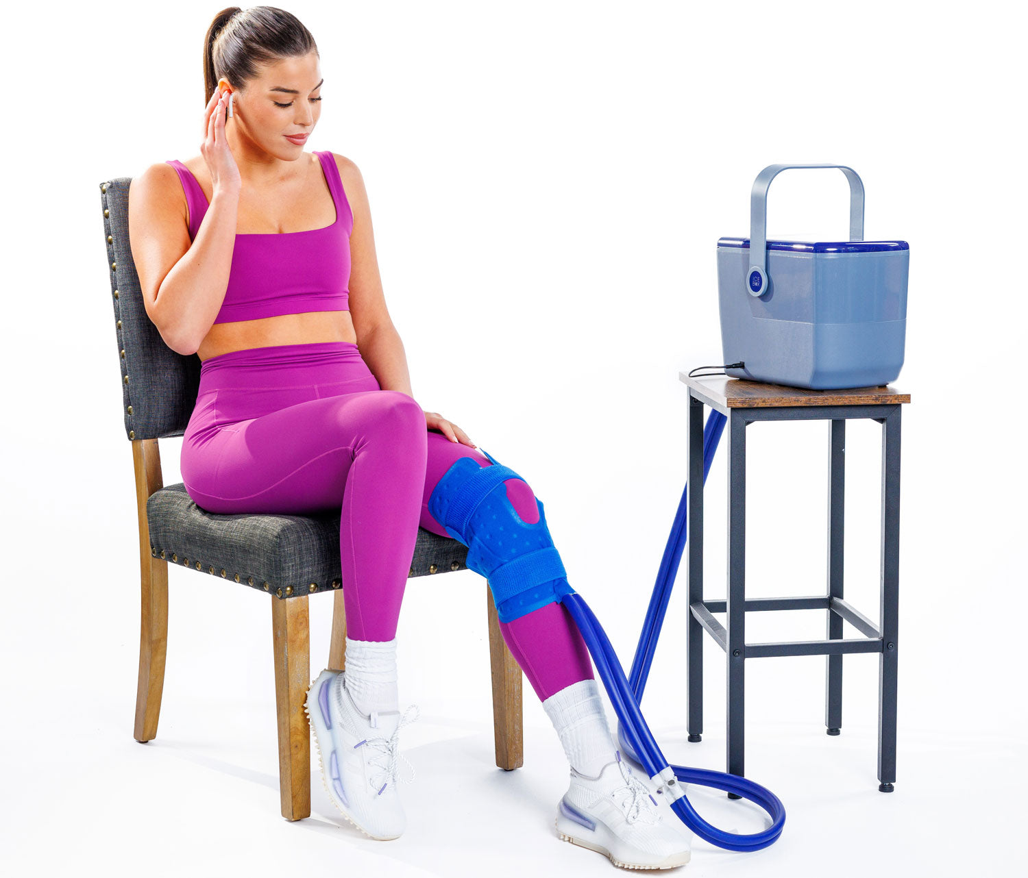 A woman seated while using the Ice Box cold therapy system with a pad on her knee.