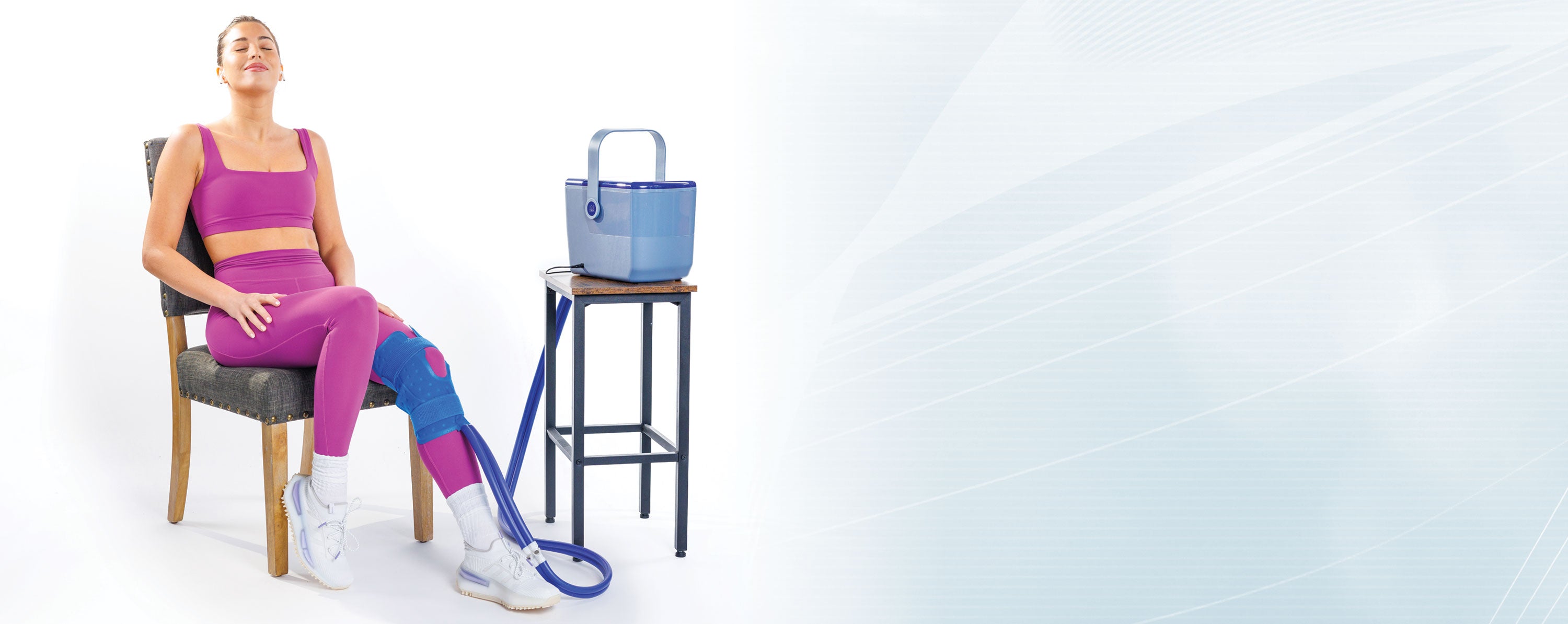 A woman seated while using the Ice Box cold therapy system with a pad on her knee.