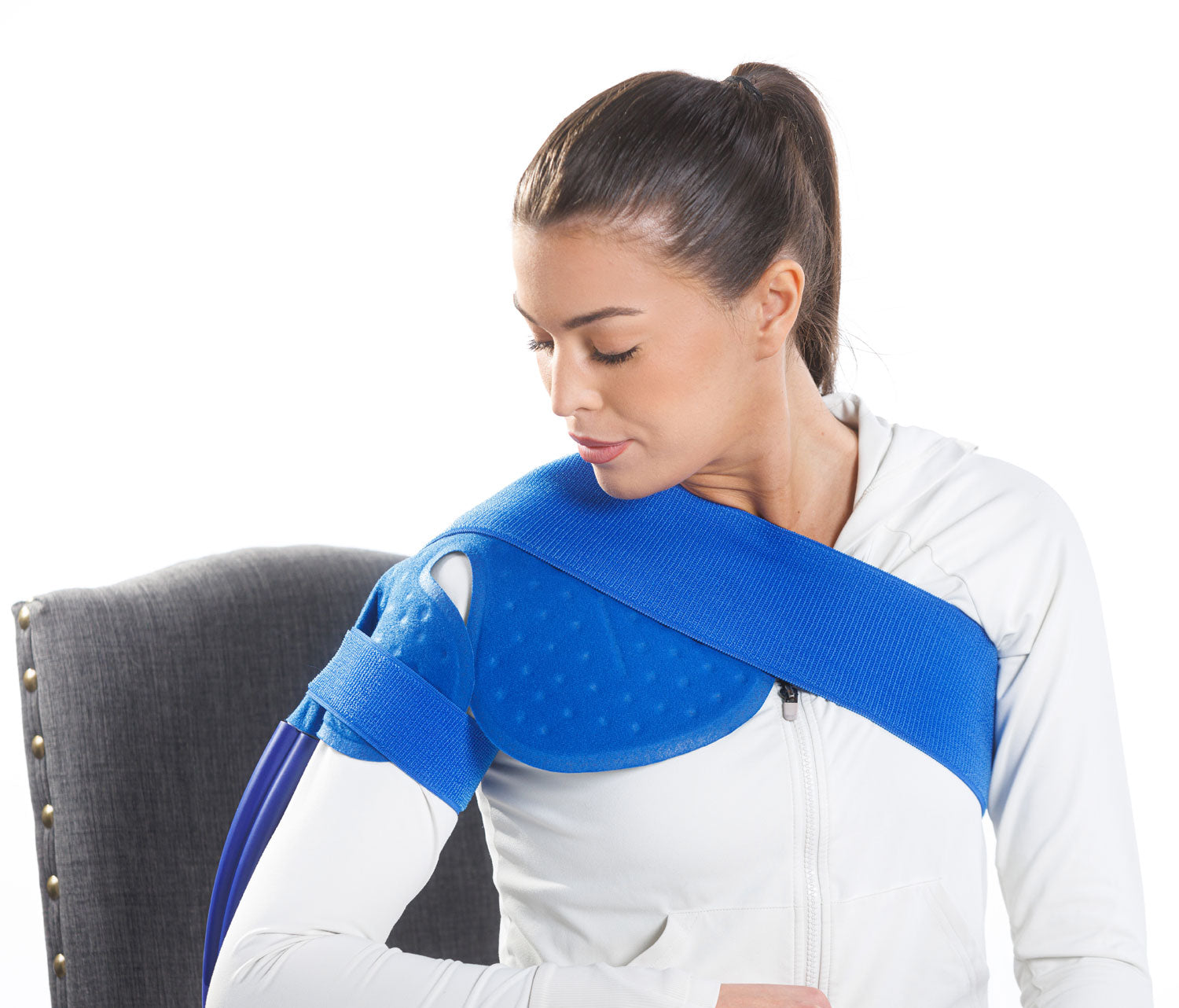 A woman seated while using the Ice Box cold therapy system with a cooling pad on her shoulder.